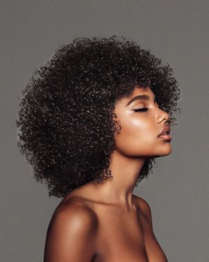 Side profile beauty portrait showcasing natural curly afro hairstyle against gray background.
