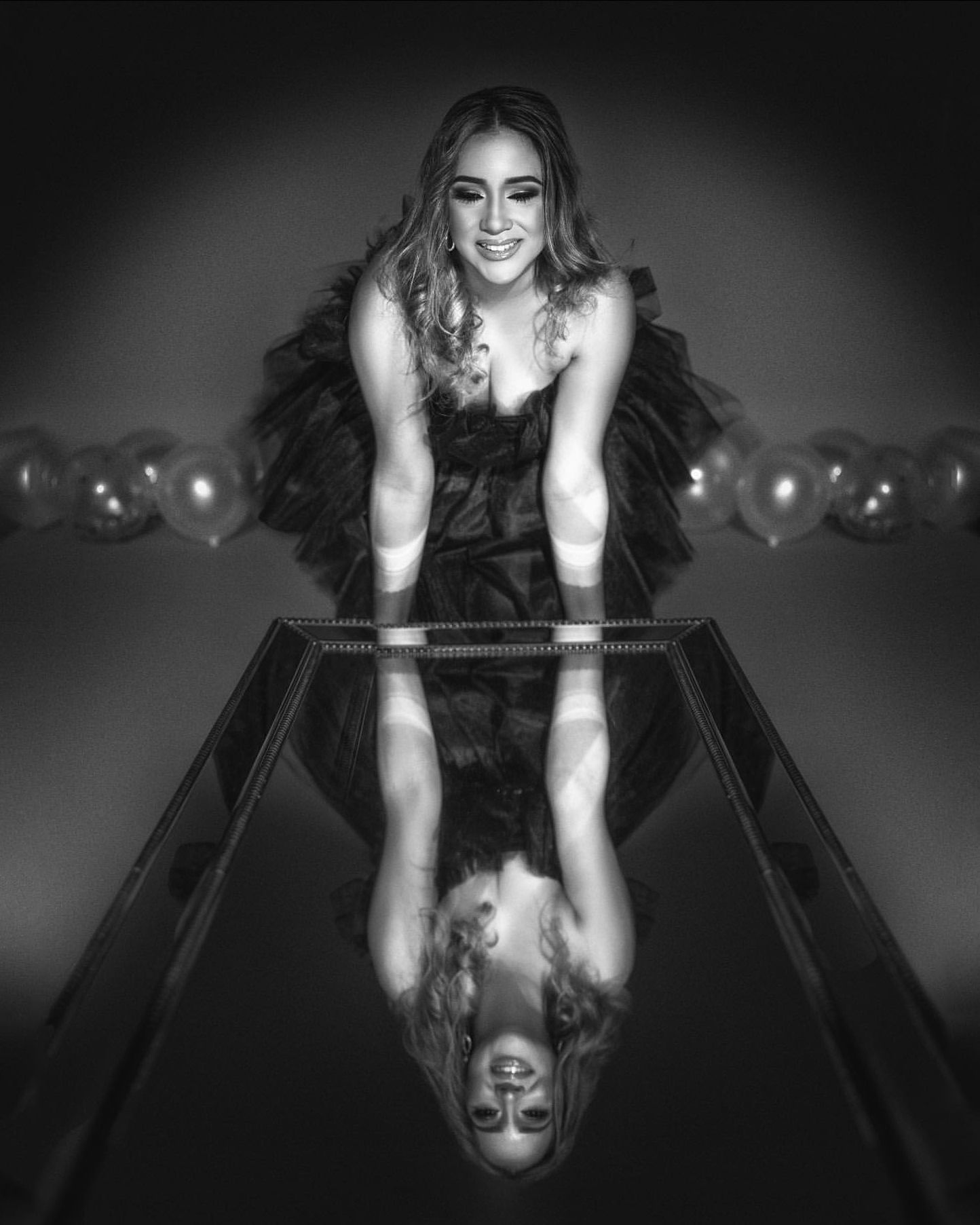 Black and white portrait with mirror reflection effect and balloons in dramatic lighting.