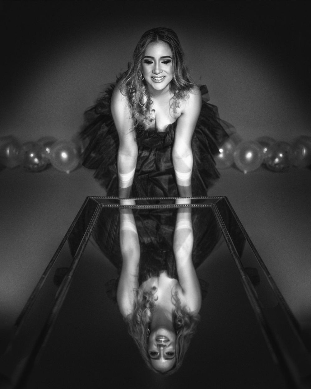 Black and white portrait with mirror reflection effect and balloons in dramatic lighting.