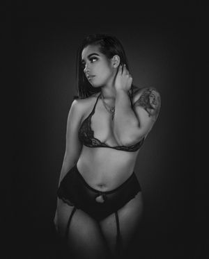 Monochrome boudoir portrait in lingerie against dark background with dramatic lighting.