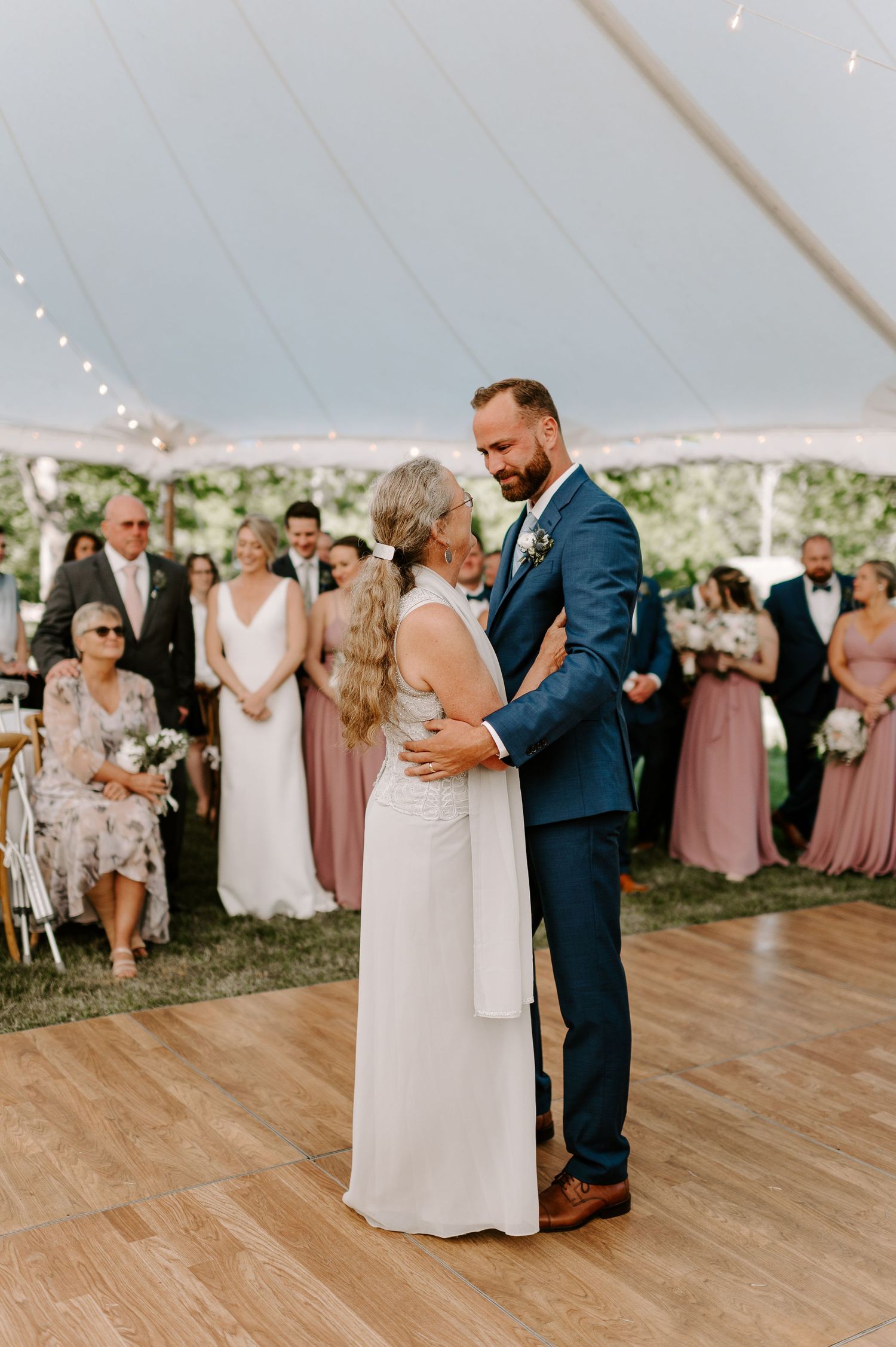 Couple shares intimate dance moment on wooden floor during outdoor tented reception.