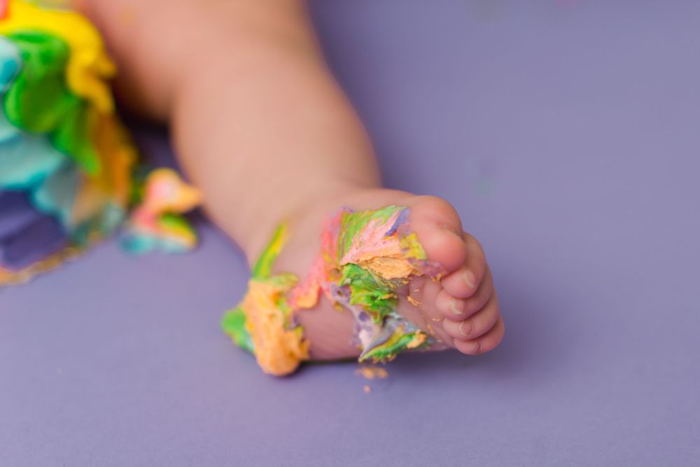 Tiny feet covered in colorful frosting against a purple background.
