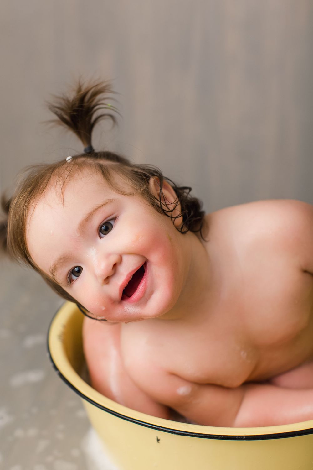 Laughing baby lying in a vintage yellow basin during bath time.