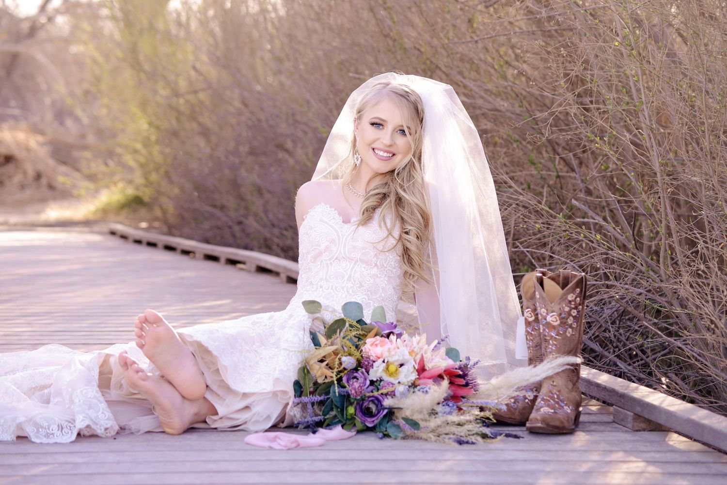 Bride in vintage-style lace dress poses gracefully on wooden boardwalk with vibrant bouquet at the i-20 wildlife preserve in Midland Texas.