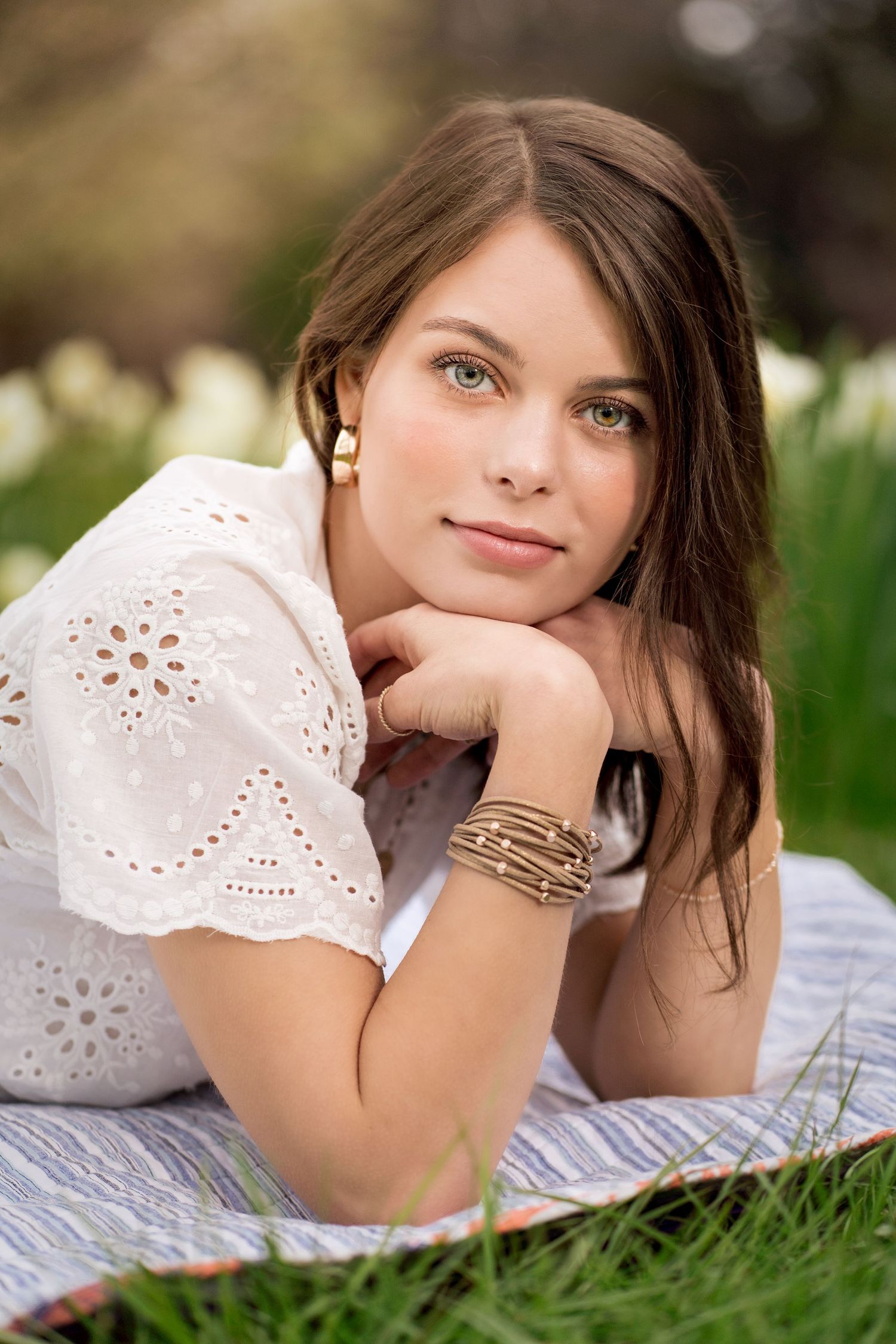 Portrait in white eyelet lace dress lying on grass with dreamy expression.