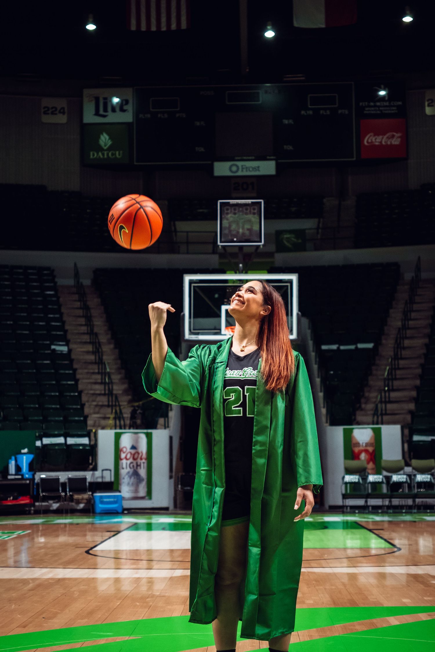 Basketball player in green uniform practicing shots in an empty arena.