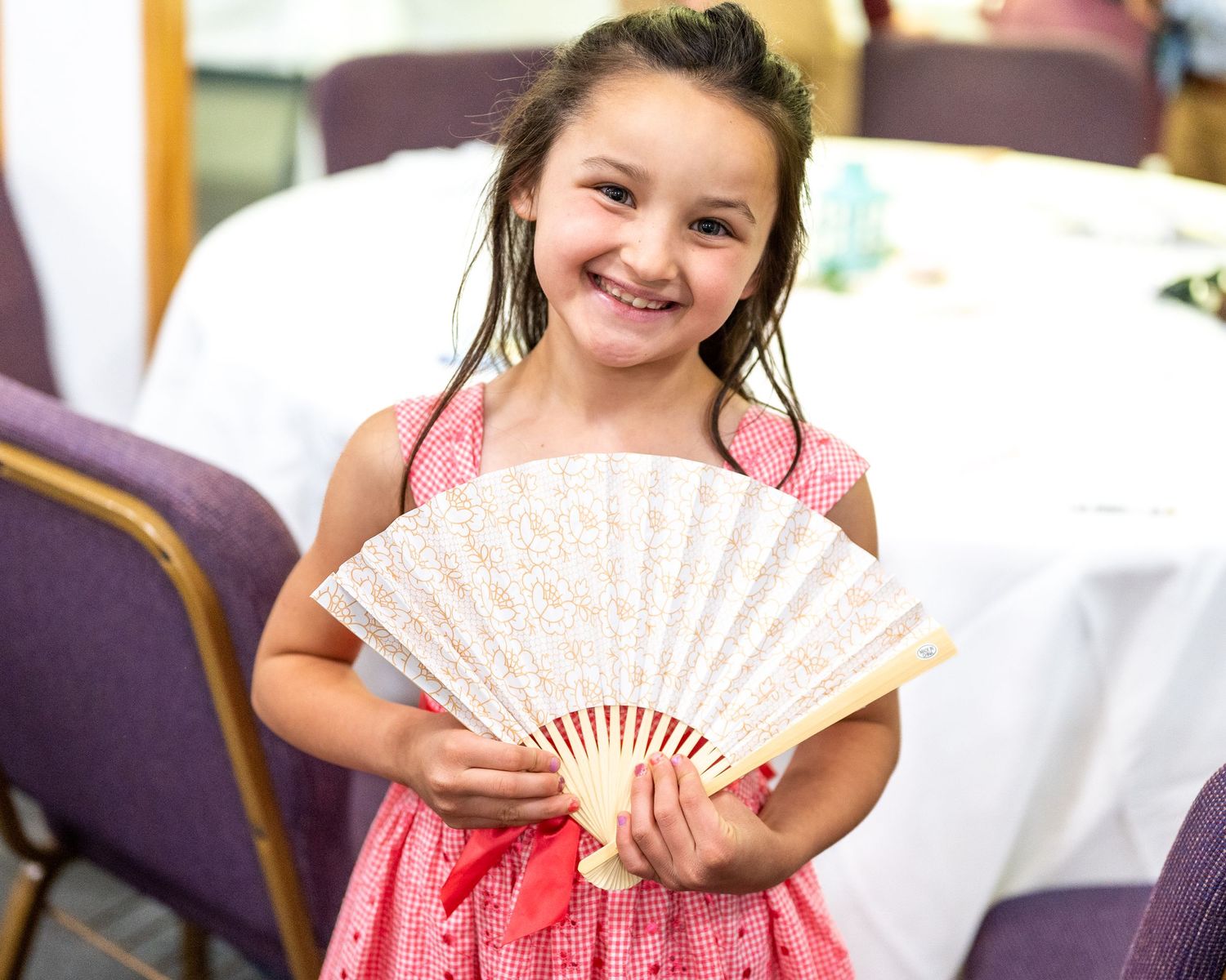 Little girl in a pink dress smiling while holding a pretty fan. Photo Credit Journeys Photo Stories.