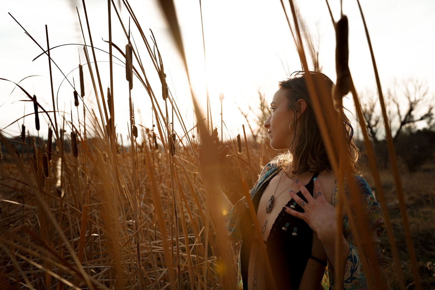 Silhouette figure standing among tall grass at golden sunset in peaceful outdoor setting.