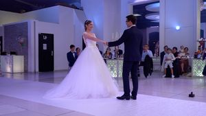 Wedding celebration in a modern white venue with guests watching the newlyweds dance.
