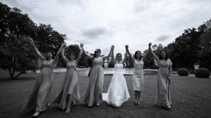 Wedding party poses with raised arms in celebration on an outdoor lawn.