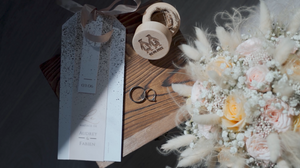 Wedding details featuring rings and delicate dried flower arrangements on wooden surface.
