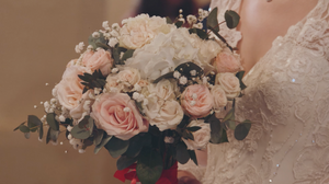 Delicate pink roses and baby's breath floral arrangement against lace wedding dress.