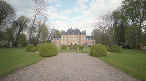 Panoramic view of a grand estate with manicured grounds and tree-lined driveway.