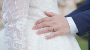 Close-up detail of white lace wedding dress with hands showing wedding ring.