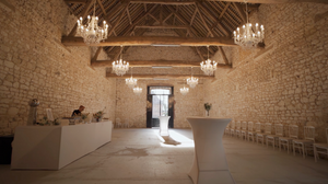 Rustic stone barn venue interior with elegant crystal chandeliers and exposed wooden beams.