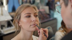 A makeup artist applies lipstick to a bride during wedding preparations.