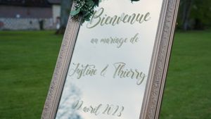 An elegant framed wedding welcome sign displayed on grass with ornate lettering.