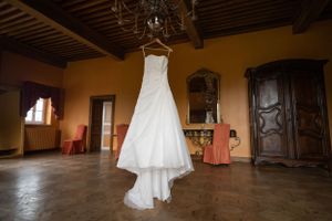 Wedding dress hanging in a rustic wooden room with natural lighting and vintage furniture.