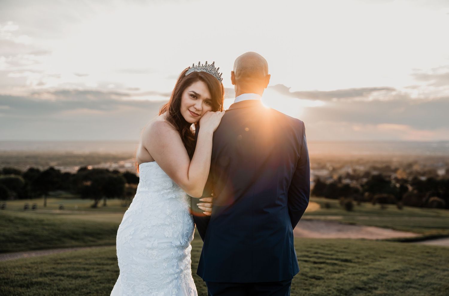 Newlyweds share intimate moment against sunset mountain backdrop.