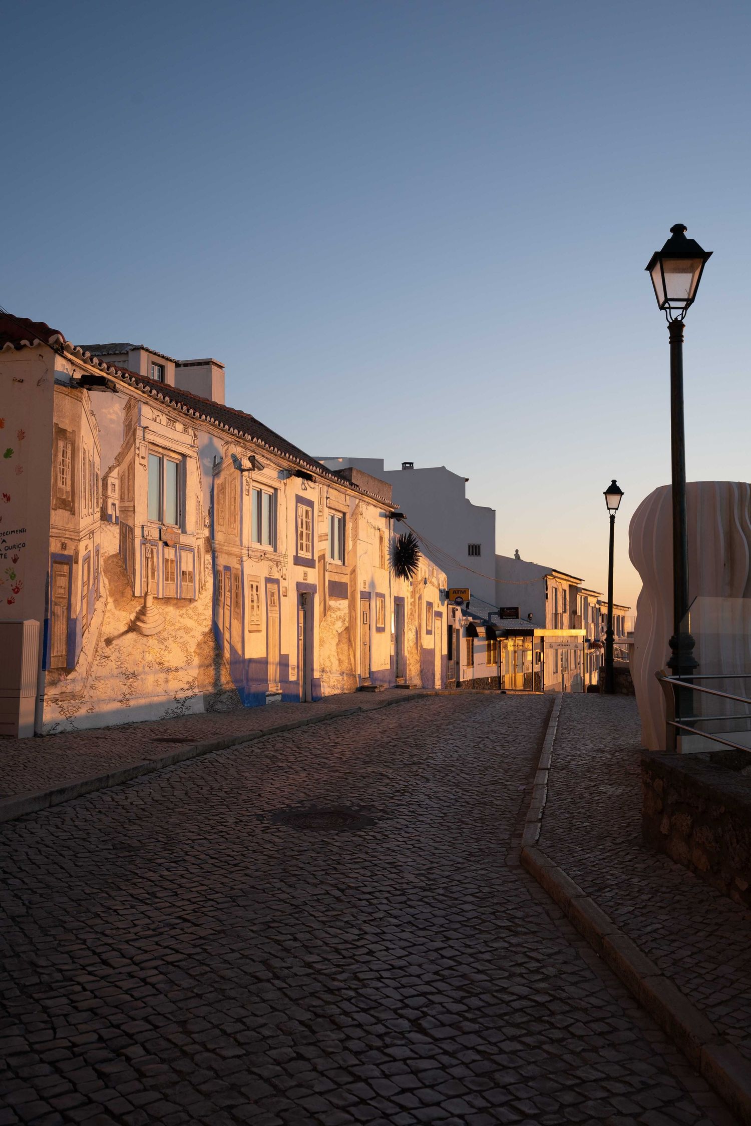 Cobblestone street with vintage lampposts and weathered buildings in warm evening light.