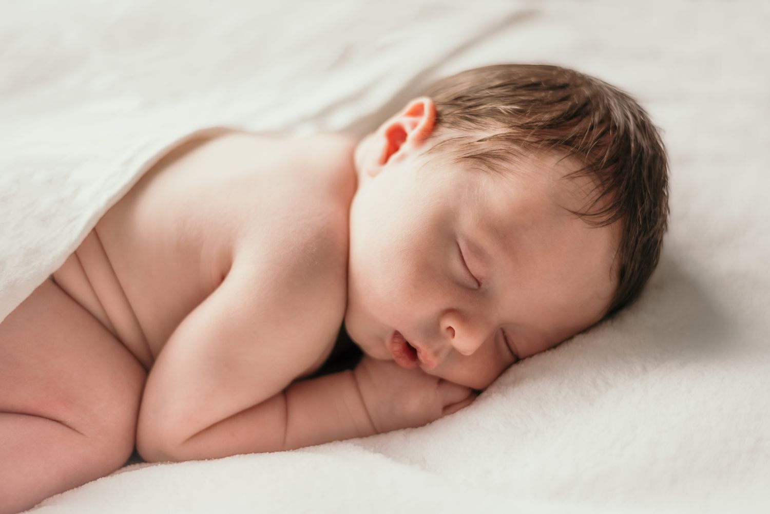 Side view of sleeping newborn on white blanket during studio photography session.