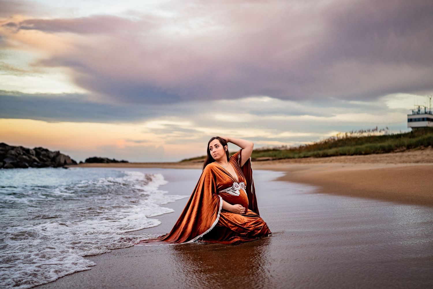 A dramatic beach portrait at sunset with flowing red fabric and coastal rocks.