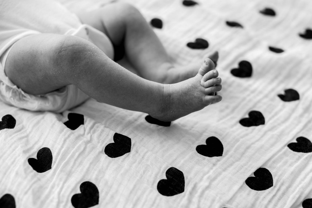 Baby feet resting on white fabric with black heart pattern.