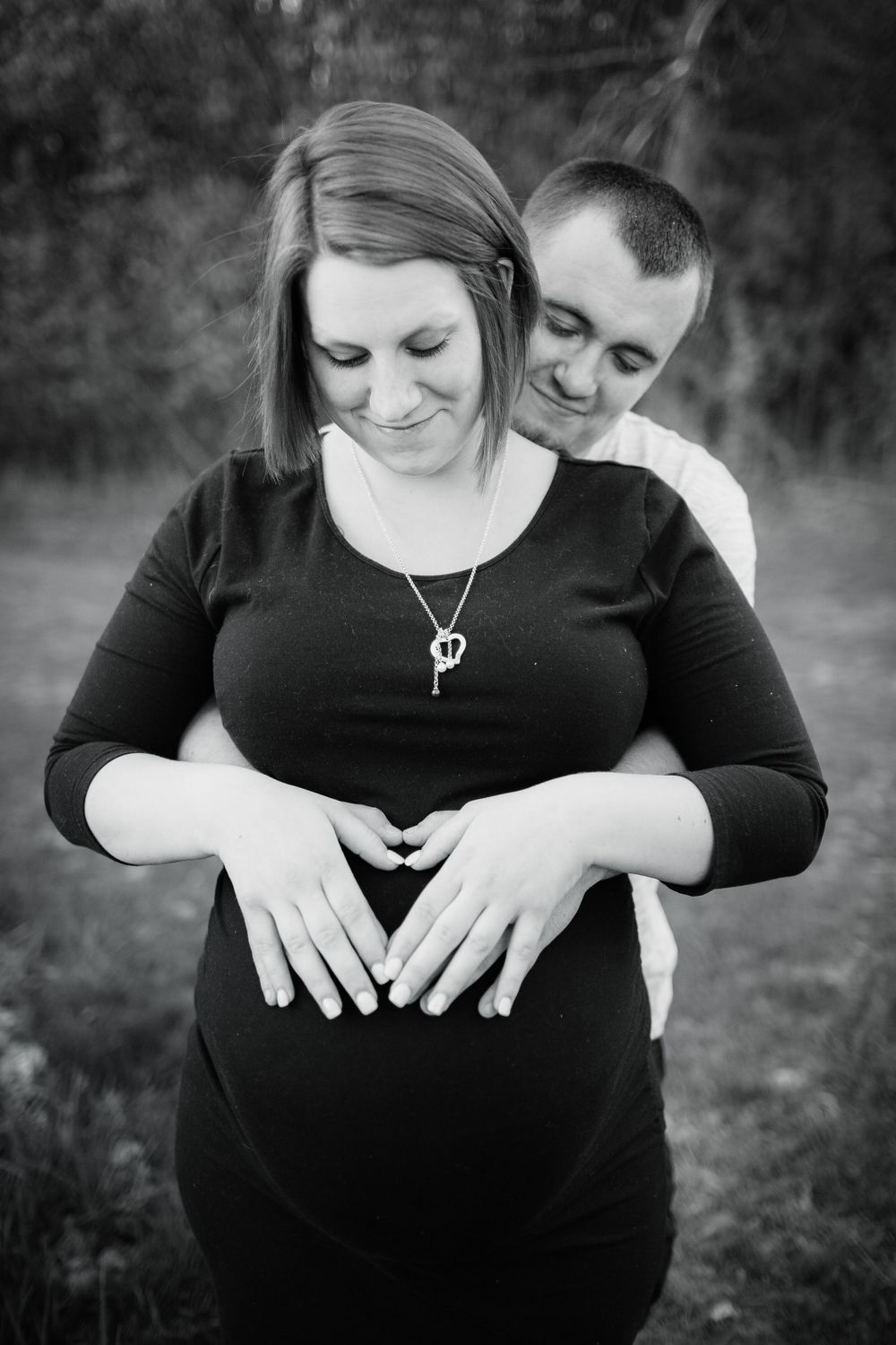 Black and white maternity photo of couple embracing outdoors.