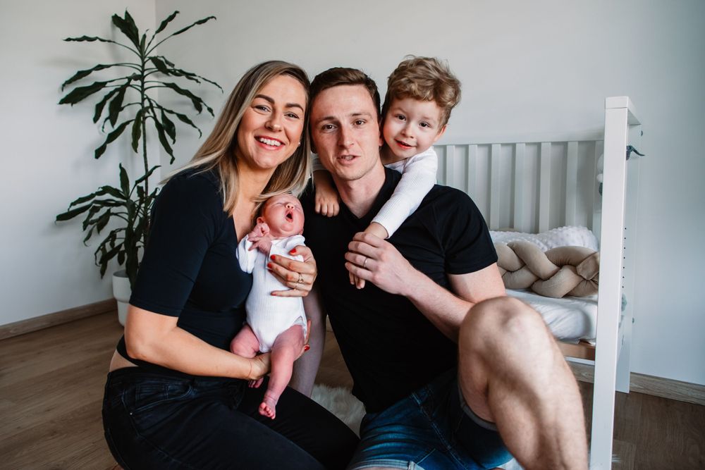Family sitting together near white crib and indoor plant.