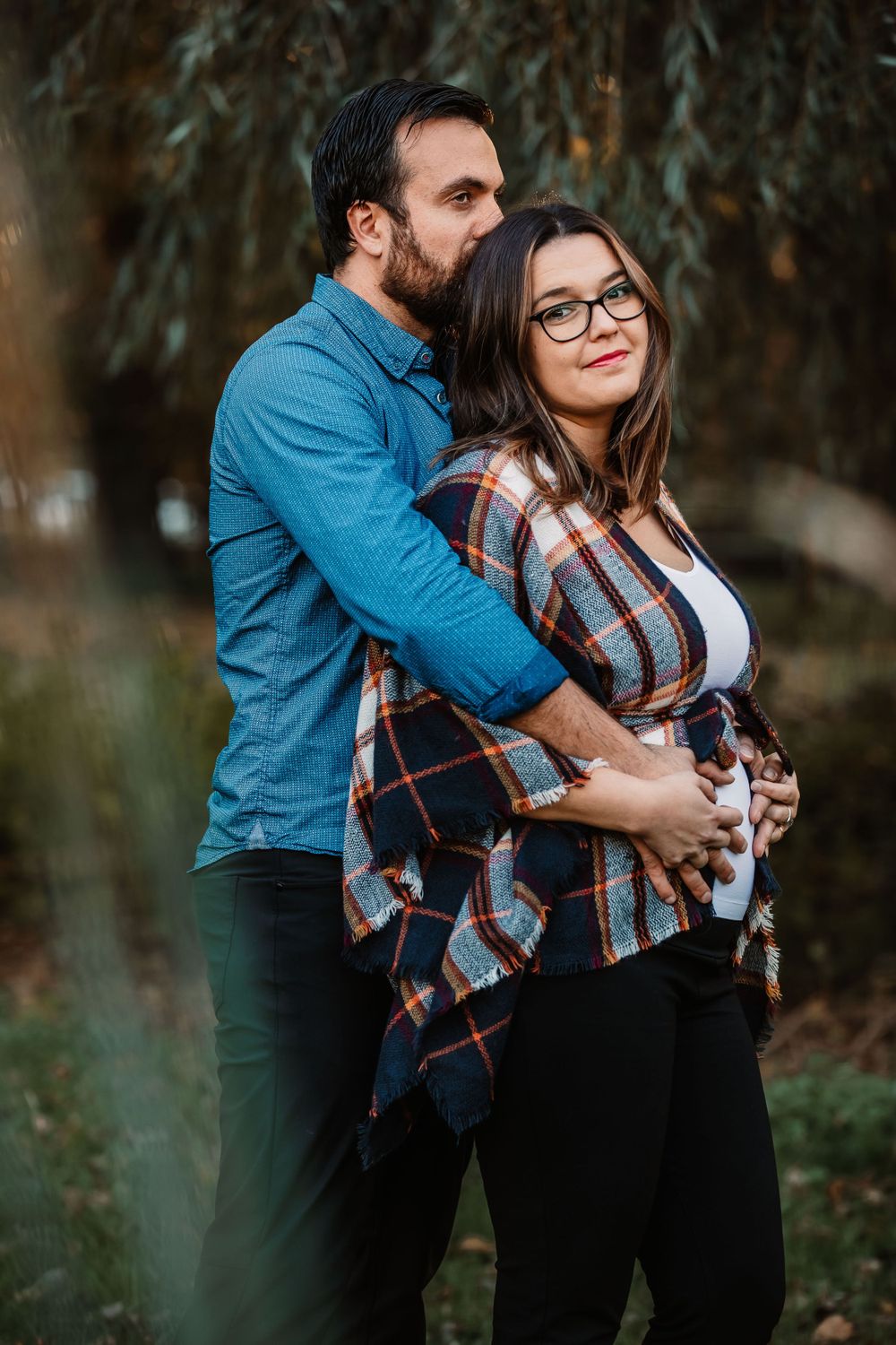 Intimate maternity portrait of couple embracing in nature wearing coordinated blue and plaid outfits.