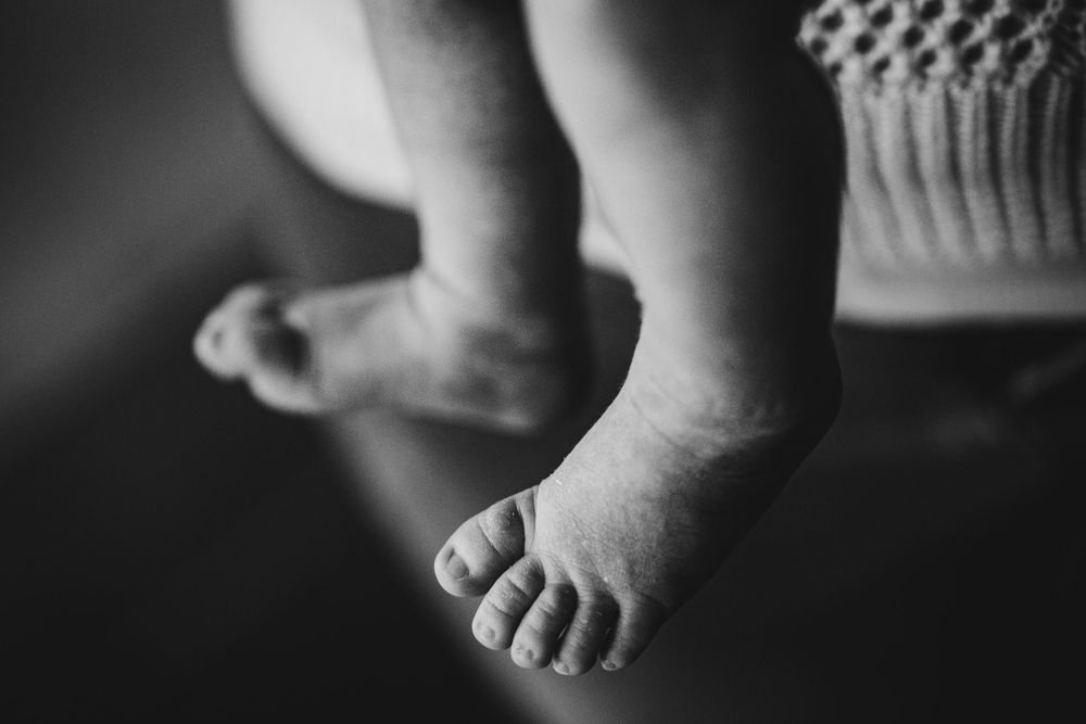 Black and white close-up photograph of tiny baby feet against a textured background.