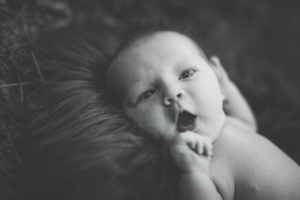 Black and white portrait of a baby lying on soft textured material with wide eyes and curious expression.