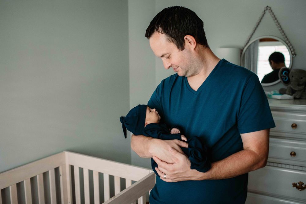 Person in navy shirt holding small infant in nursery setting.
