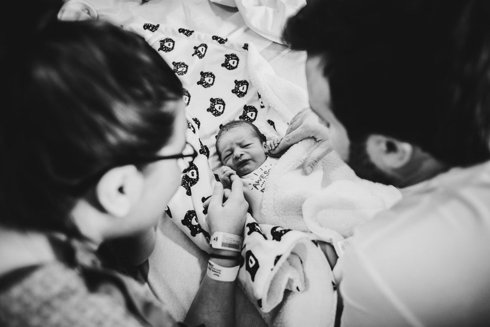Black and white photo of a newborn baby wearing patterned clothing during a tender moment.
