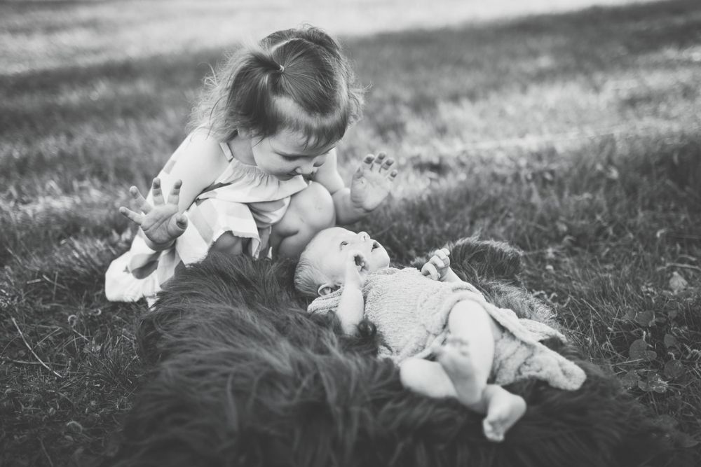 Black and white photo of siblings bonding on grass.