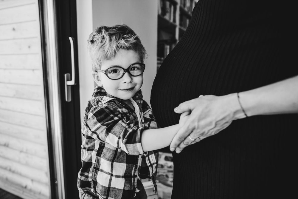 Child in plaid shirt and glasses reaches for hand in black and white portrait.