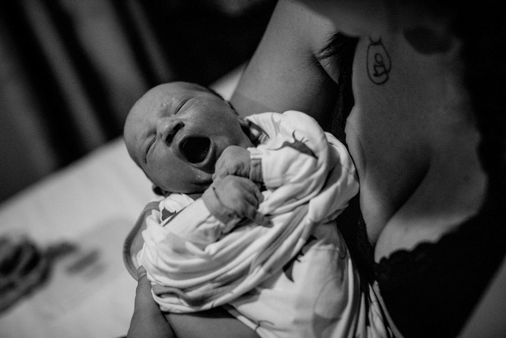 Black and white image of a newborn baby wrapped in a white blanket yawning.