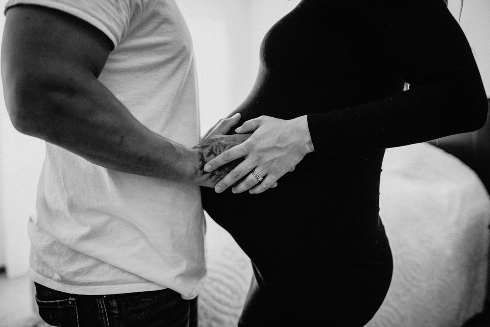 Black and white photo of hands gently resting on a pregnant belly.