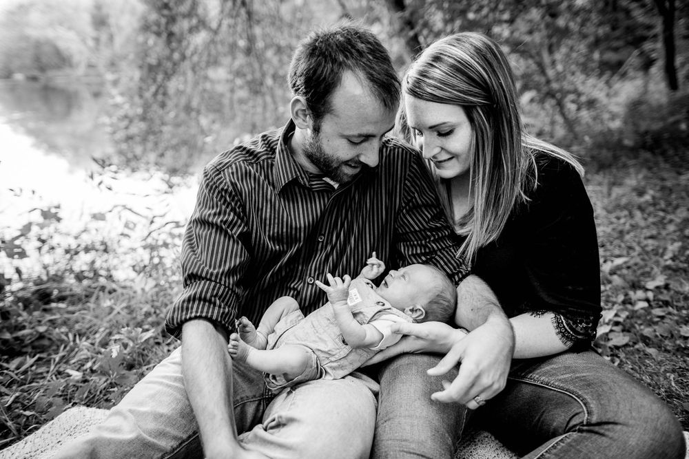 Black and white photo of family sharing intimate moment with baby outdoors.