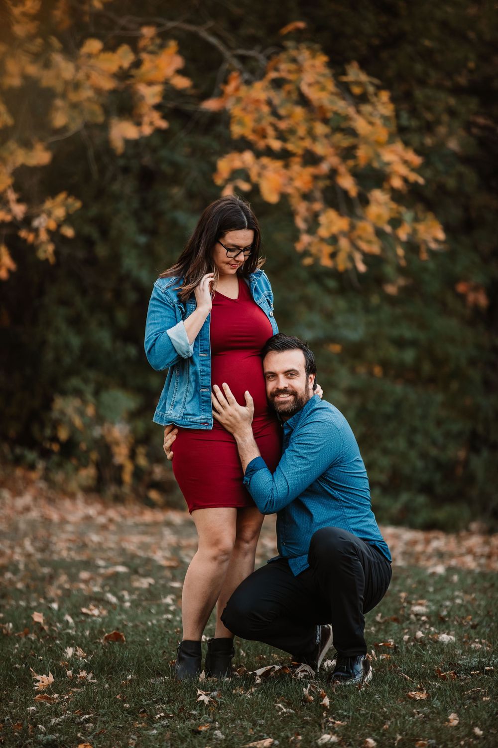 Maternity photo showing couple in matching denim with autumn leaves in background.