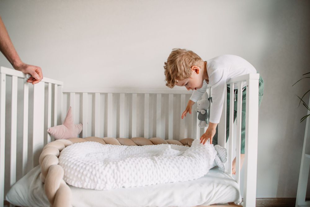Child standing in white crib reaching towards edge with enthusiasm.