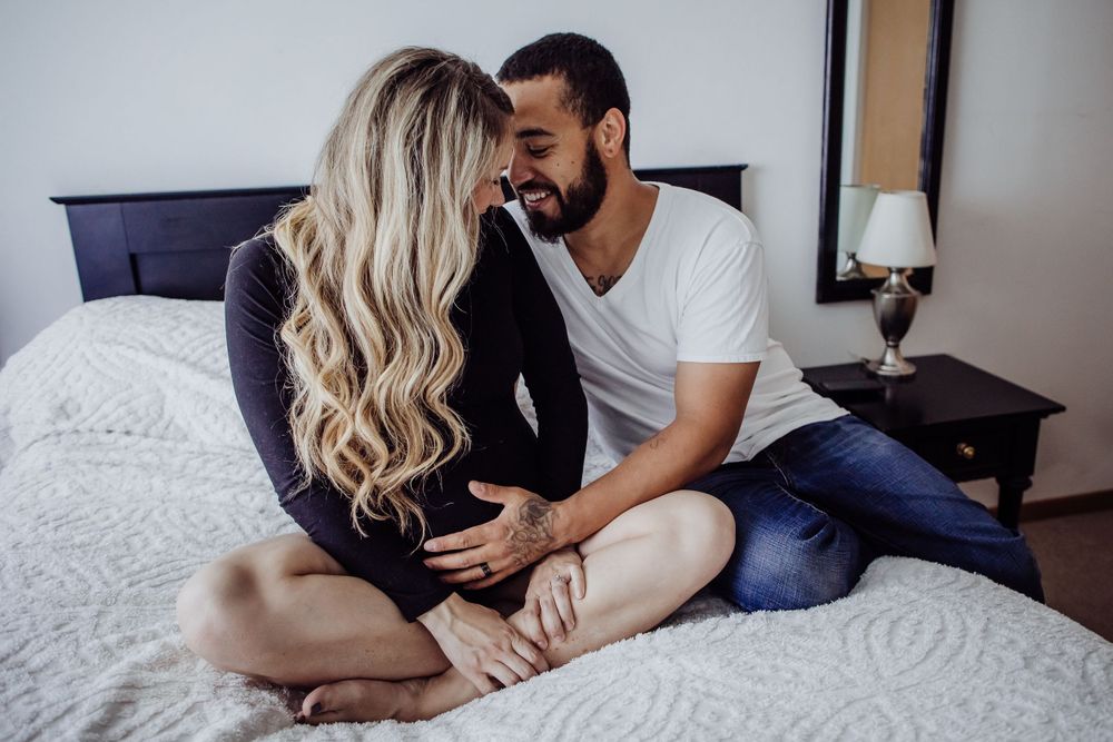 Couple sharing intimate moment during maternity photoshoot on bed.