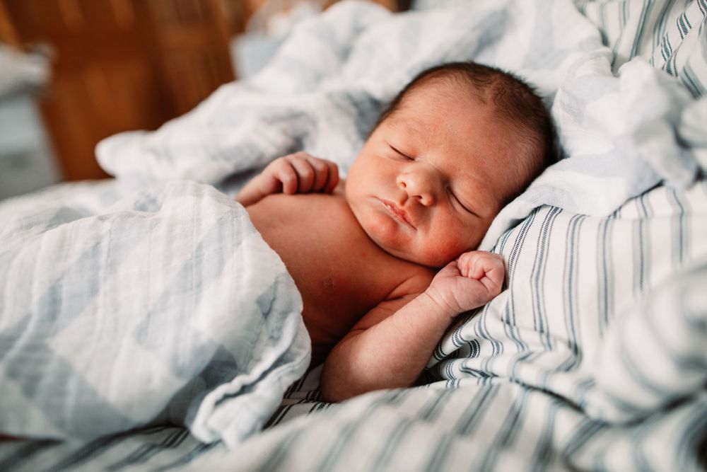Peaceful sleeping newborn on blue striped bedding in natural window light.