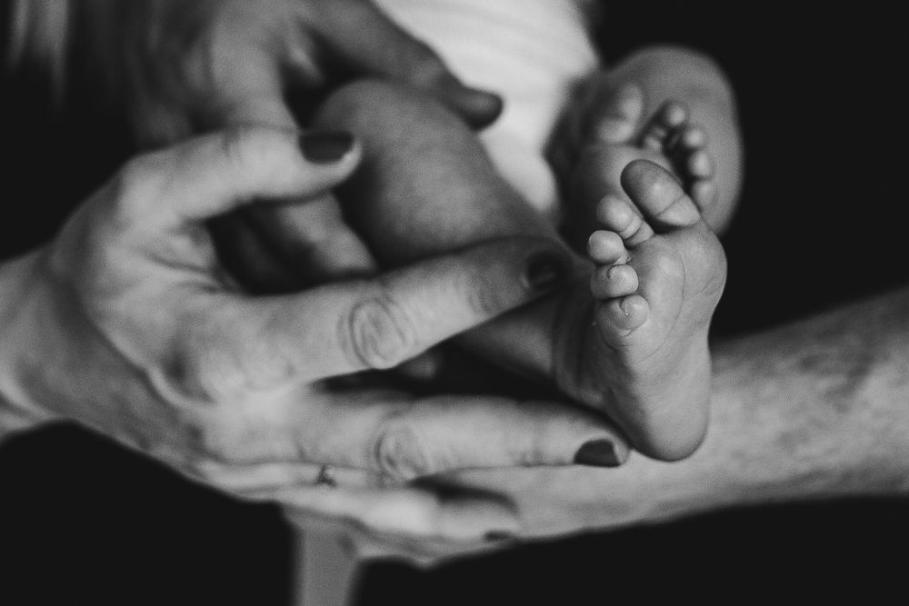 Black and white close-up of tiny newborn foot held in adult hands.