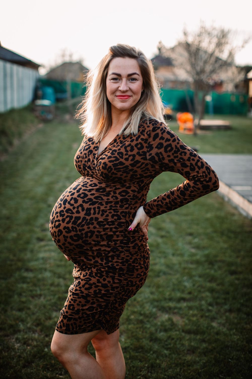 Maternity portrait outdoors featuring leopard print dress against garden background.