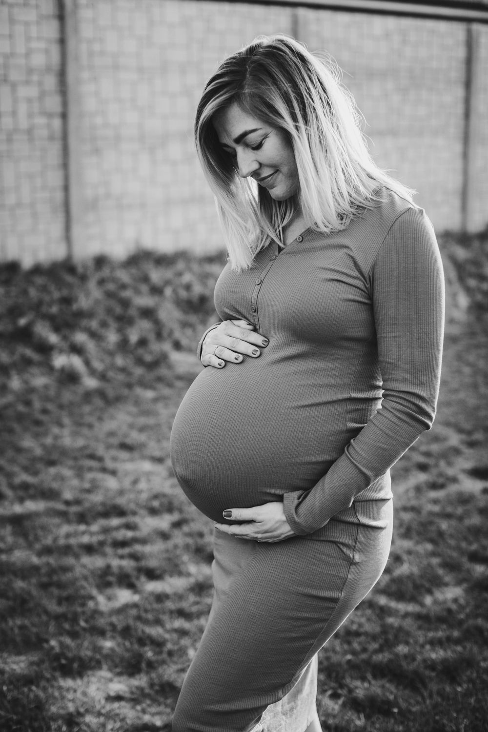 Maternity portrait in black and white showing pregnant woman cradling belly in fitted dress.