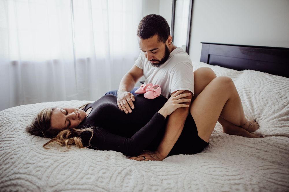 Couple lying on bed during intimate maternity photoshoot.
