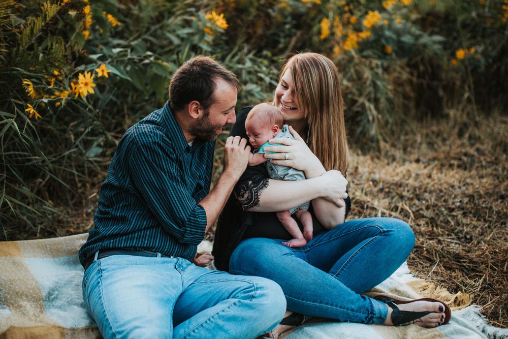 Family sitting on blanket outdoors sharing tender moment with infant.