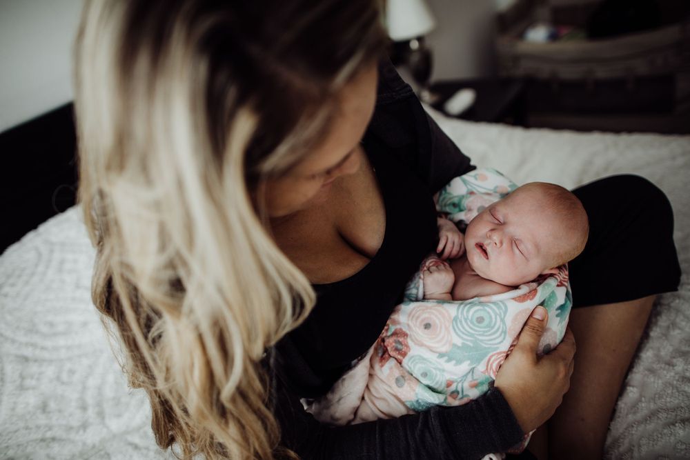 Mother cradling sleeping newborn baby in intimate lifestyle photo.