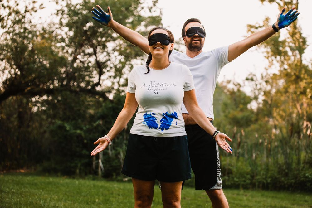 Couple with blue-painted hands raised in celebration during an outdoor gender reveal moment.